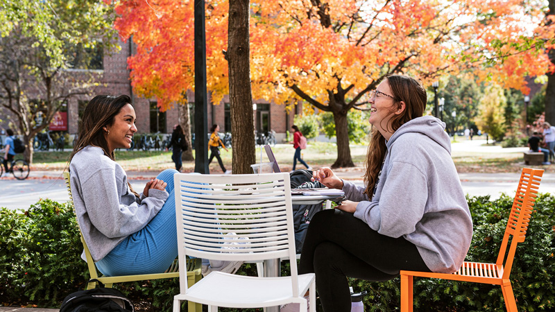 Two women sitting together and laughing around an outdoor table.